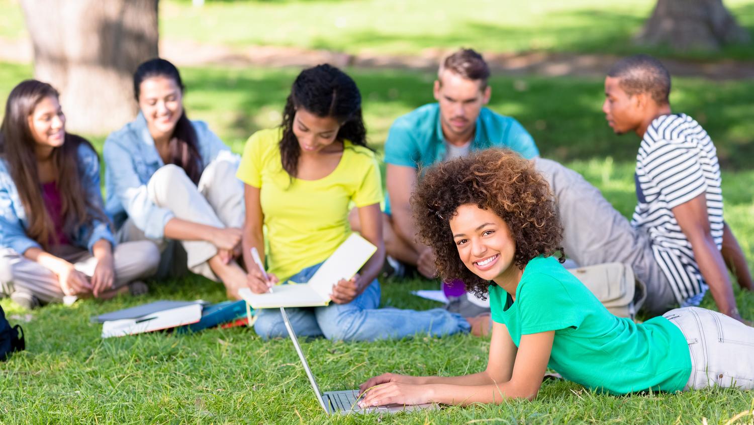 Estudiantes universitarios estudiando y socializando en el césped del campus en un día soleado de verano. Estudiantes universitarios estudiando y socializando en el césped del campus en un día soleado de verano.