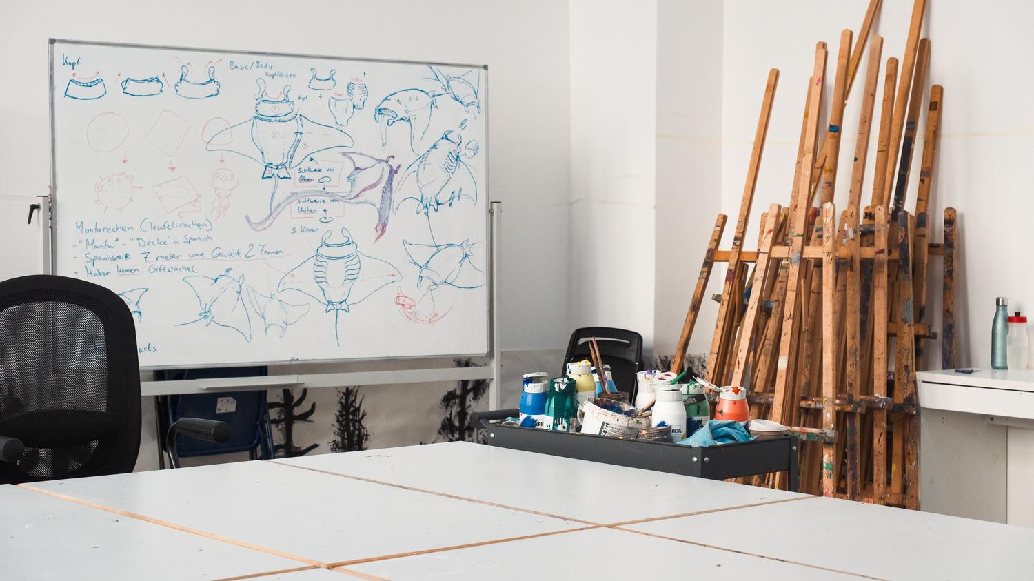 Estudio de arte creativo con caballetes y bocetos en una pizarra, representando el entorno laboral de las enseñanzas artísticas. Estudio de arte creativo con caballetes y bocetos en una pizarra, representando el entorno laboral de las enseñanzas artísticas.