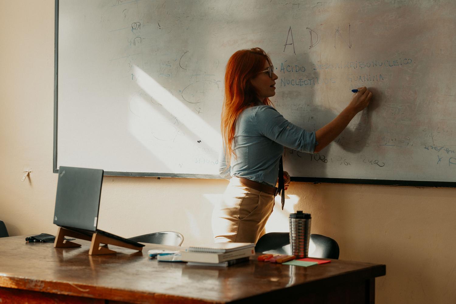 Profesora impartiendo lección en la pizarra blanca durante su fase de prácticas Profesora impartiendo lección en la pizarra blanca durante su fase de prácticas