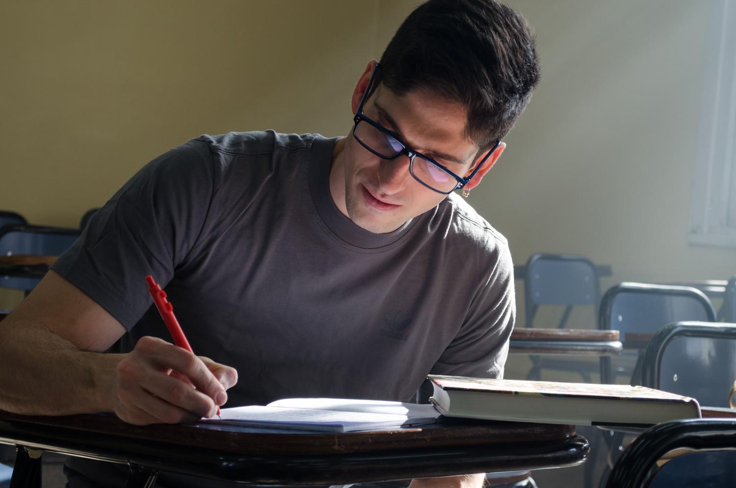 Estudiante concentrado estudiando el temario de oposiciones en un aula vacía Estudiante concentrado estudiando el temario de oposiciones en un aula vacía