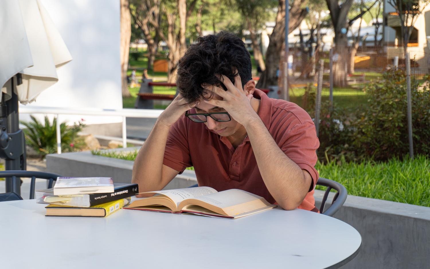 Estudiante universitario abrumado por los libros en un entorno al aire libre, representando el estrés académico. Estudiante universitario abrumado por los libros en un entorno al aire libre, representando el estrés académico.