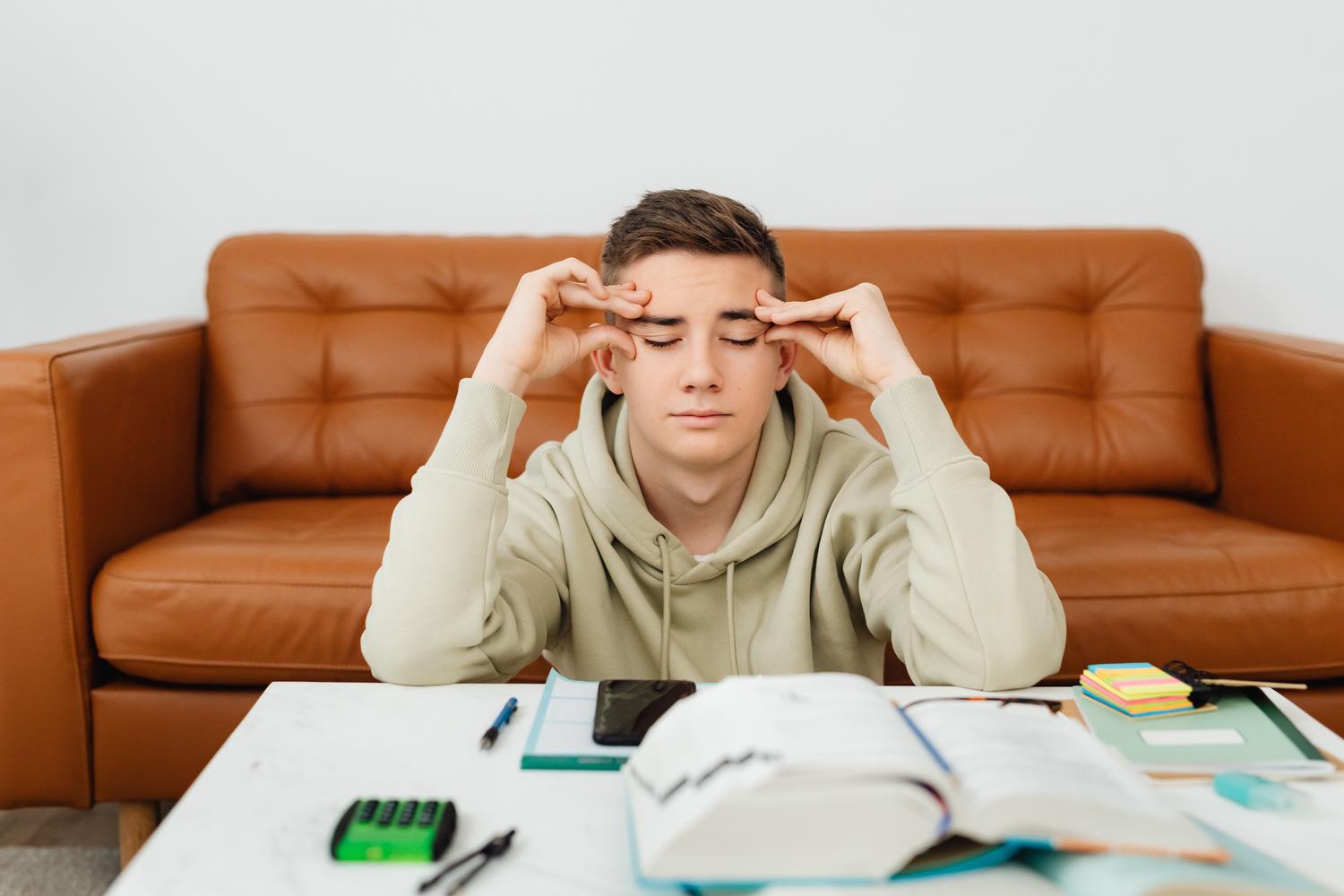 Joven estudiando en casa con gesto de estrés y fatiga mental, rodeado de libros y material de estudio. Joven estudiando en casa con gesto de estrés y fatiga mental, rodeado de libros y material de estudio.