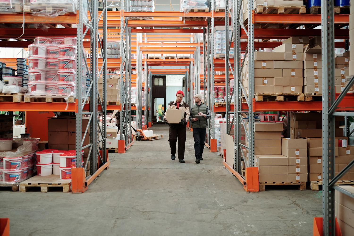 Logística y canales de distribución indirecta Trabajadores organizando paquetes en un almacén industrial espacioso, representando la logística y los canales de distribución indirecta.