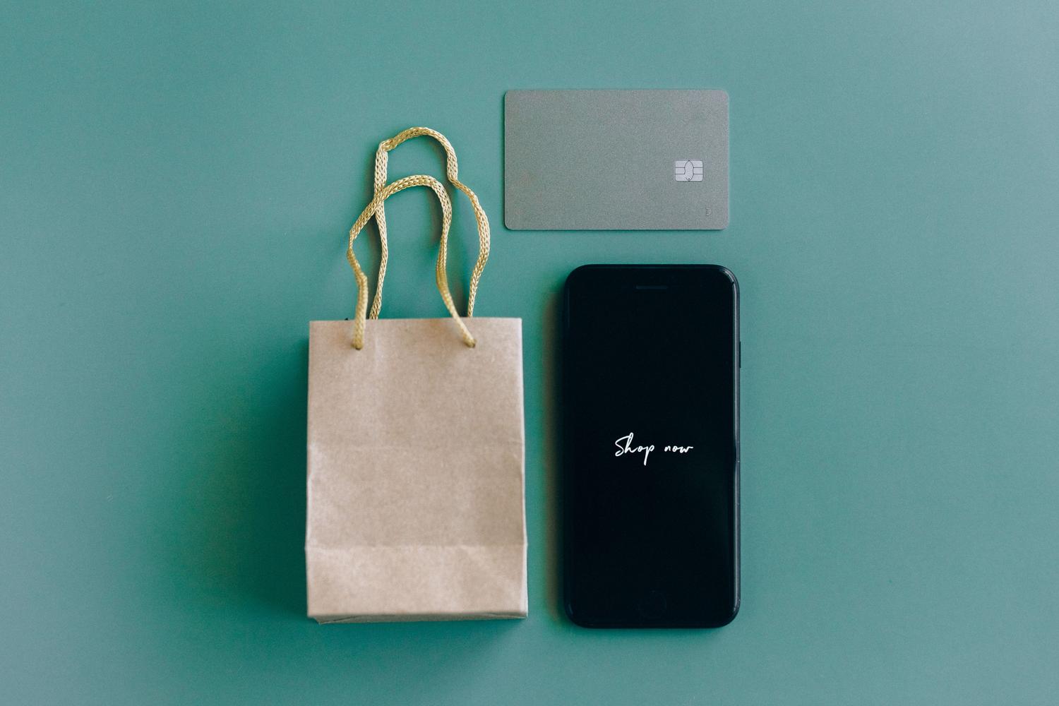 Social commerce y compras impulsivas desde el móvil Primer plano de un smartphone con el texto 'Shop now' junto a una tarjeta de crédito, ejemplificando el social commerce y las compras impulsivas.