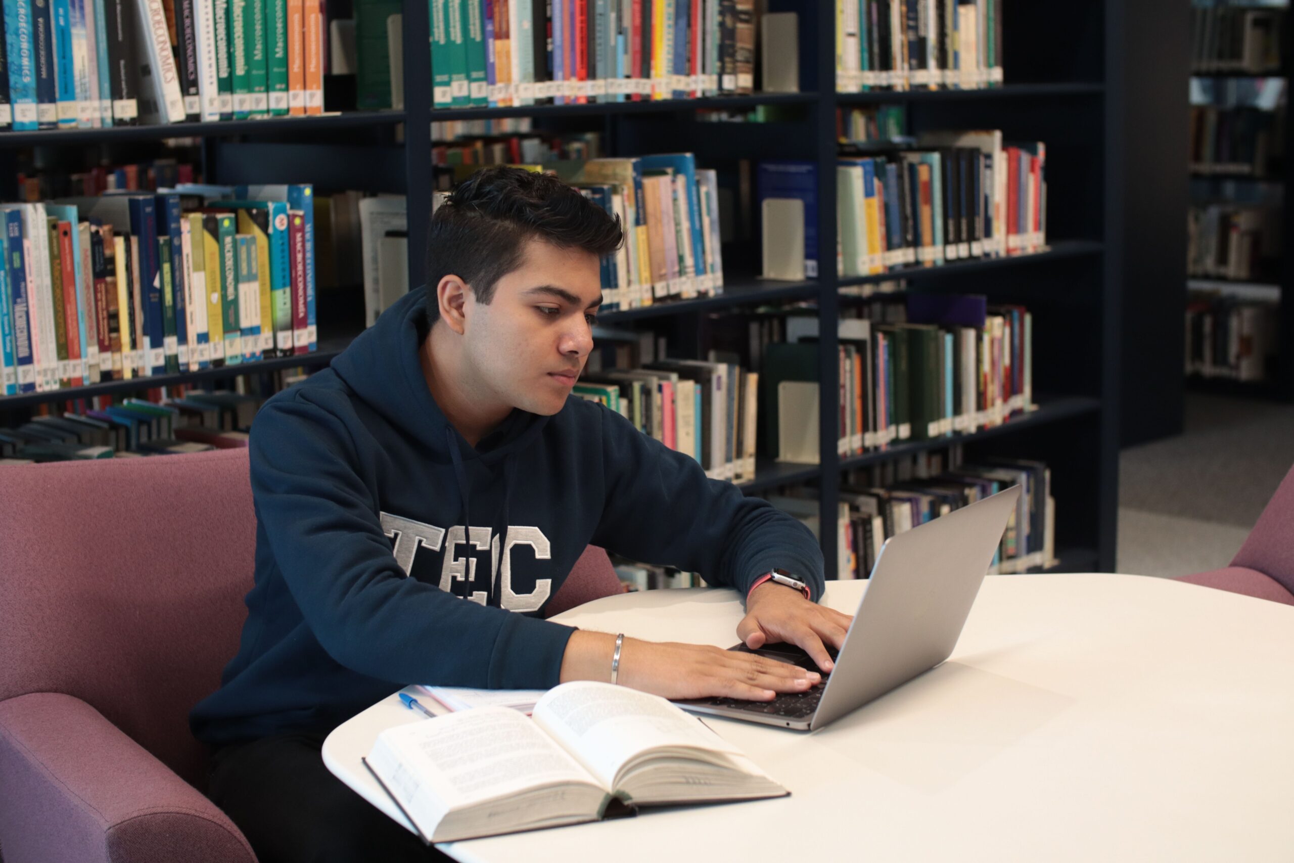 Estudiante en una biblioteca utilizando un ordenador portátil y libros de texto para investigar y redactar un trabajo académico Estudiante en una biblioteca utilizando un ordenador portátil y libros de texto para investigar y redactar un trabajo académico