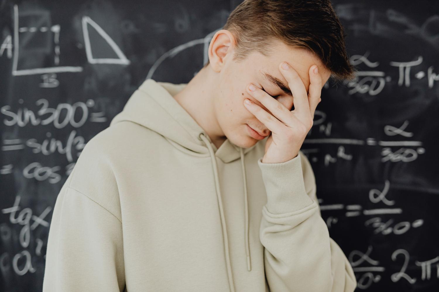 Un estudiante joven se siente abrumado frente a una pizarra llena de cálculos matemáticos, representando la frustración académica como causa del absentismo. Un estudiante joven se siente abrumado frente a una pizarra llena de cálculos matemáticos, representando la frustración académica como causa del absentismo.