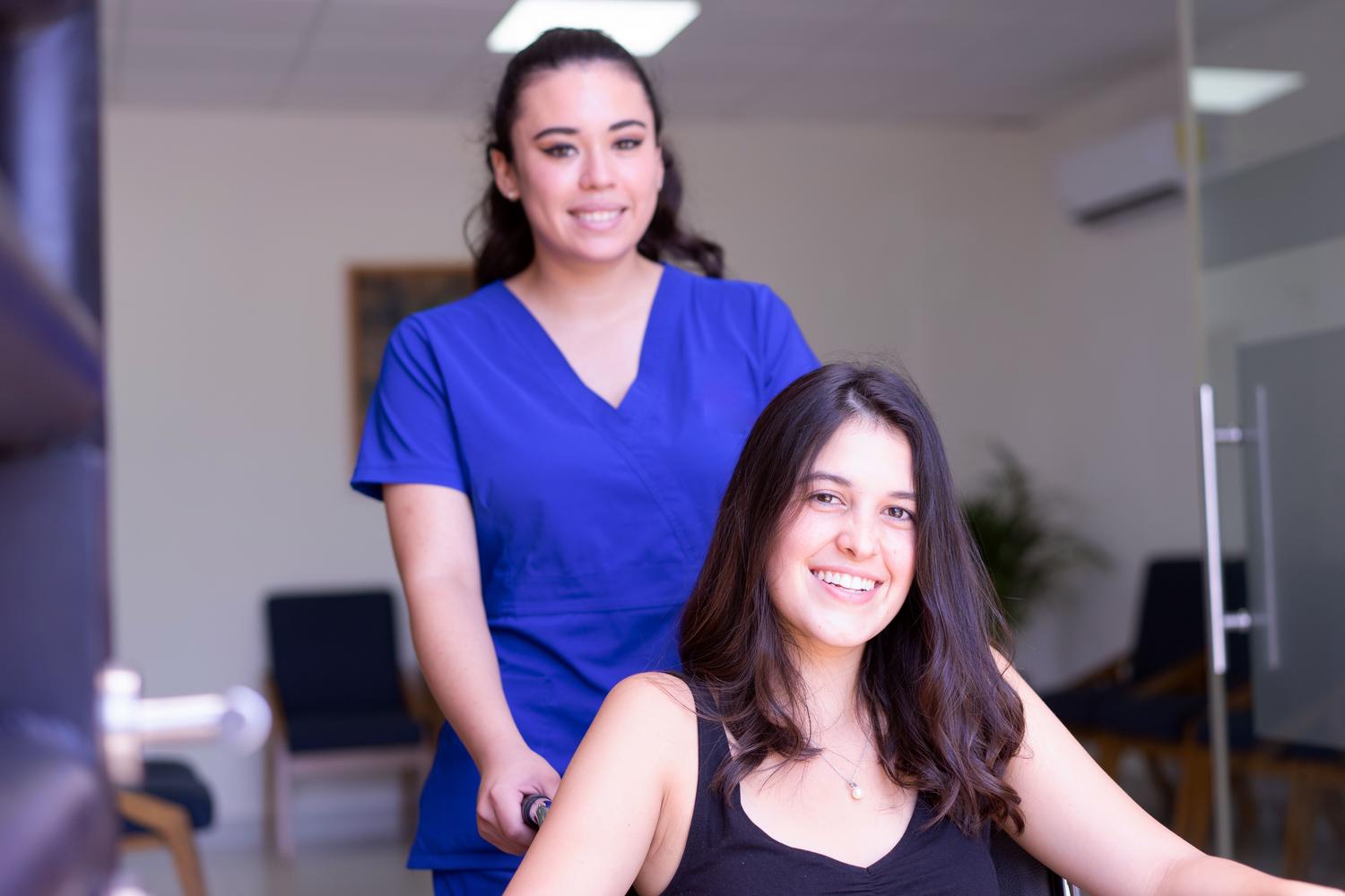 Profesional sanitaria acompañando a una paciente en silla de ruedas en un entorno clínico moderno. Profesional sanitaria acompañando a una paciente en silla de ruedas en un entorno clínico moderno.