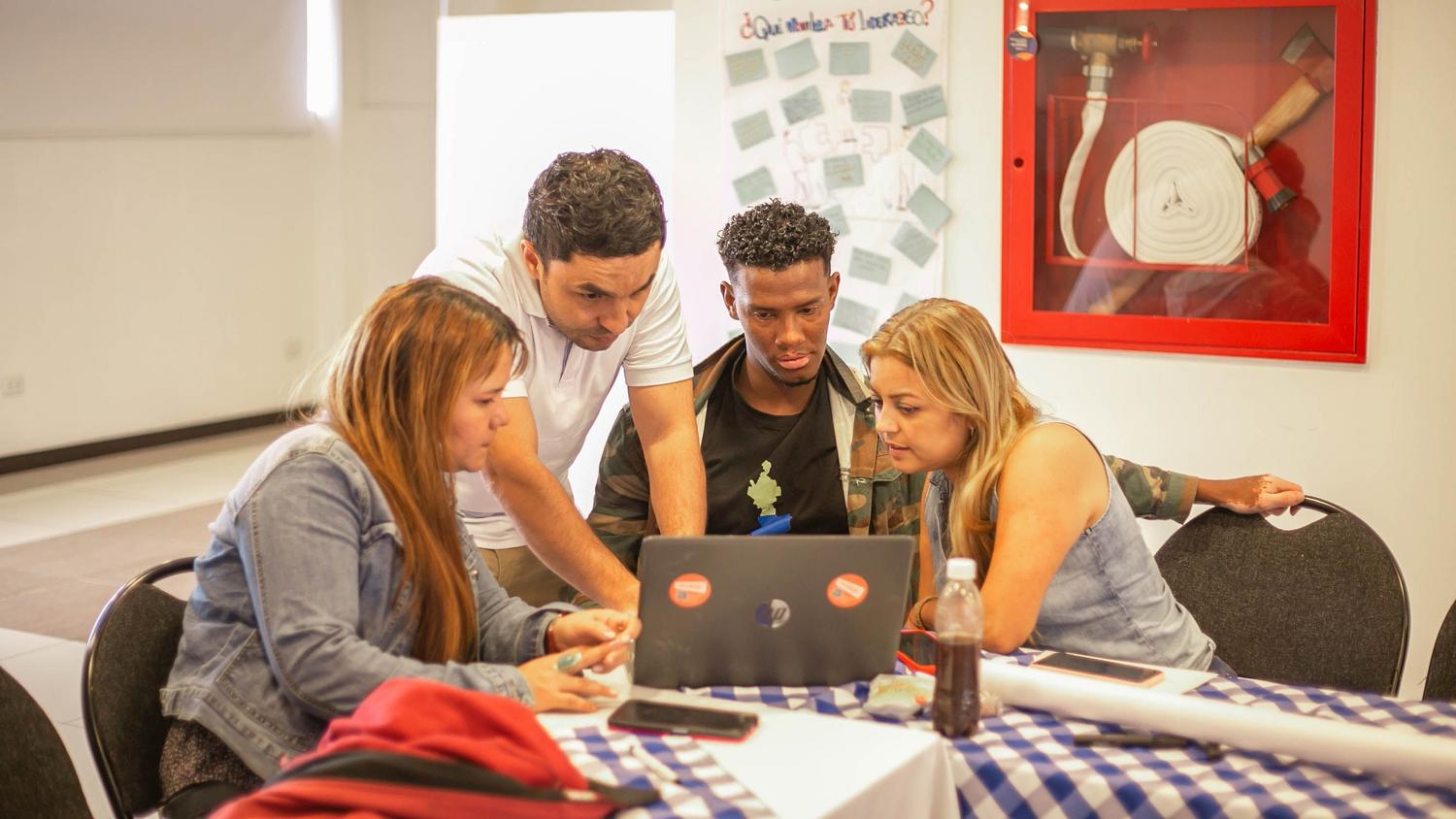 Grupo diverso de profesionales colaborando alrededor de un portátil, simbolizando el desarrollo de competencias transversales y habilidades blandas. Grupo diverso de profesionales colaborando alrededor de un portátil, simbolizando el desarrollo de competencias transversales y habilidades blandas.