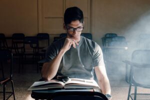 Estudiante concentrado leyendo un libro en un aula universitaria iluminada, representando el rigor académico tradicional.