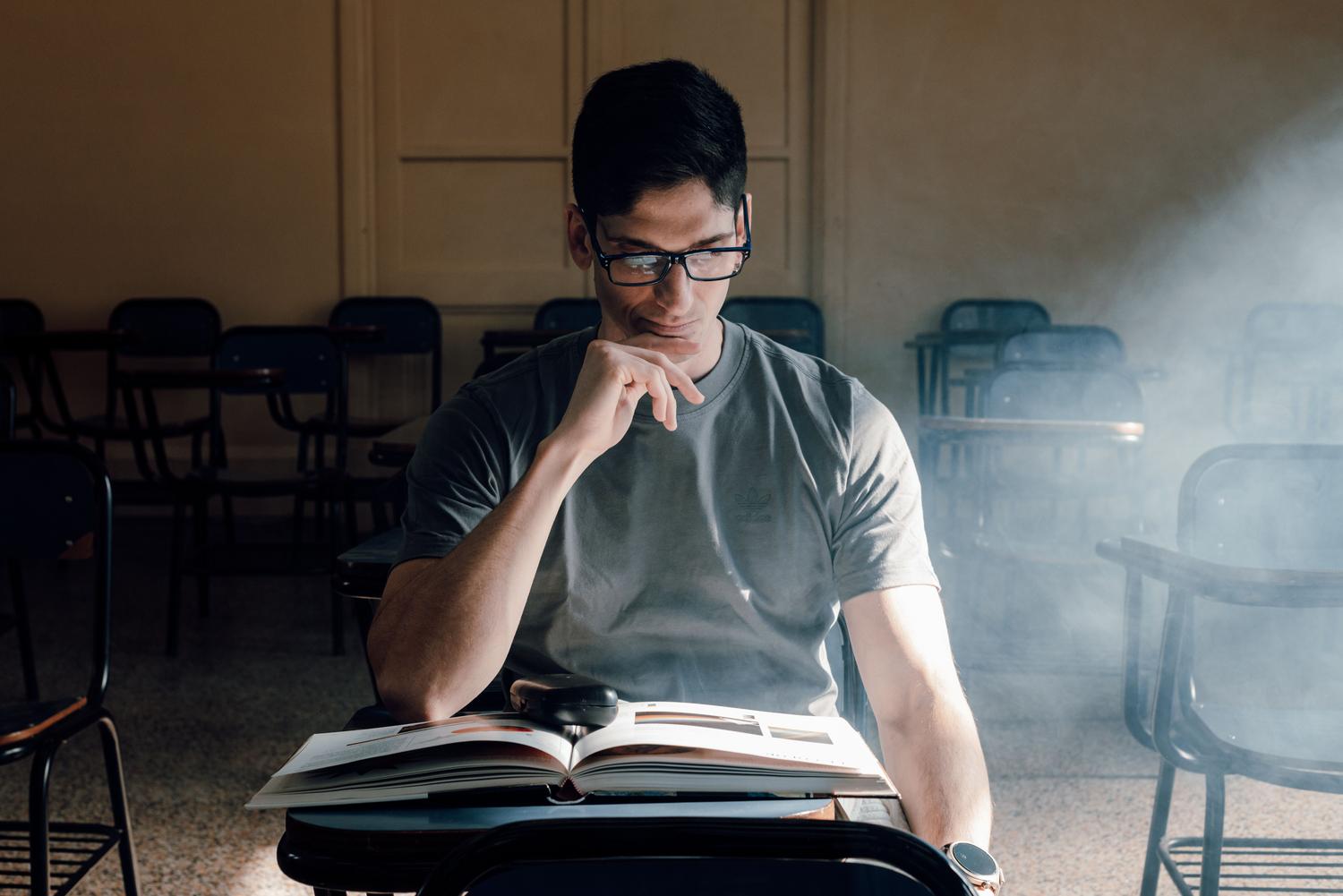 Estudiante concentrado leyendo un libro en un aula universitaria iluminada, representando el rigor académico tradicional. Estudiante concentrado leyendo un libro en un aula universitaria iluminada, representando el rigor académico tradicional.