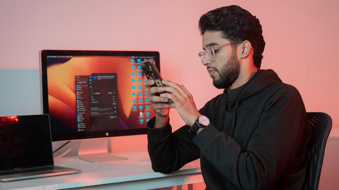 Profesional utilizando un smartphone y un ordenador en su escritorio, representando la gestión de comunidades y la interacción con usuarios. Profesional utilizando un smartphone y un ordenador en su escritorio, representando la gestión de comunidades y la interacción con usuarios.