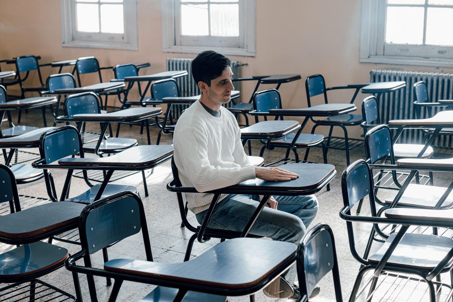Alumno solitario rodeado de pupitres vacíos en un aula, ilustrando la crisis demográfica y el sistema educativo zombi Alumno solitario rodeado de pupitres vacíos en un aula, ilustrando la crisis demográfica y el sistema educativo zombi
