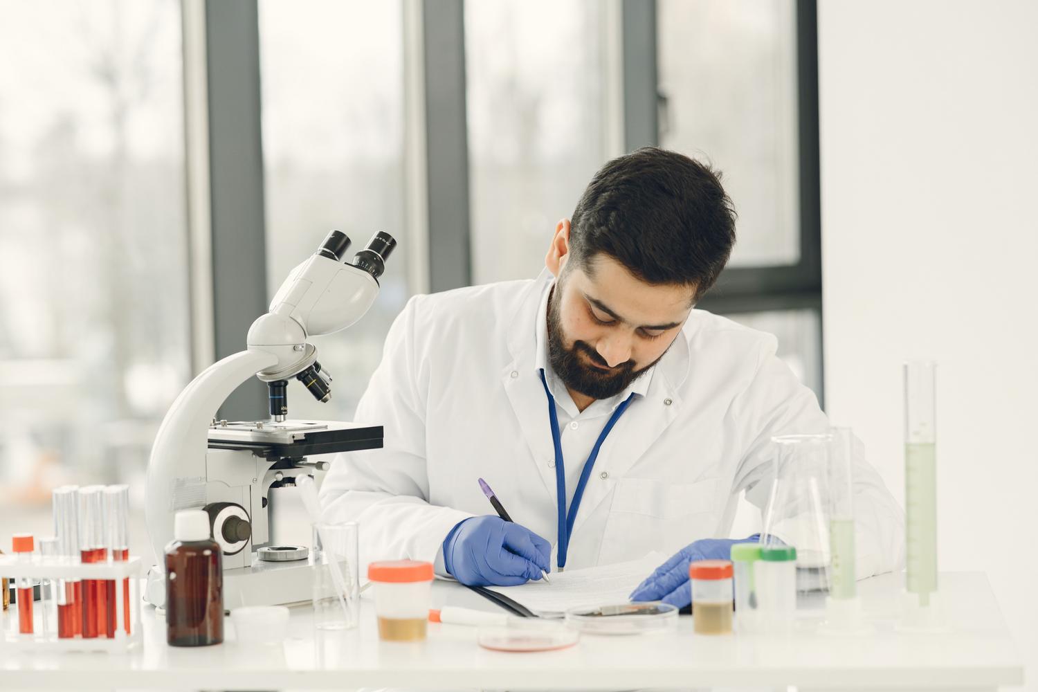 Científico tomando notas junto a un microscopio en un laboratorio, simbolizando la actividad investigadora necesaria para los sexenios. Científico tomando notas junto a un microscopio en un laboratorio, simbolizando la actividad investigadora necesaria para los sexenios.