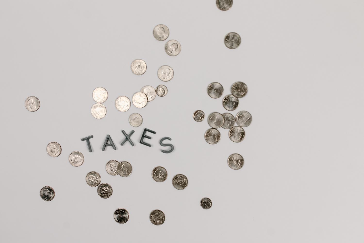 Primer plano de monedas con la palabra 'Taxes' sobre fondo blanco, representando el concepto general de impuestos. Primer plano de monedas con la palabra 'Taxes' sobre fondo blanco, representando el concepto general de impuestos.
