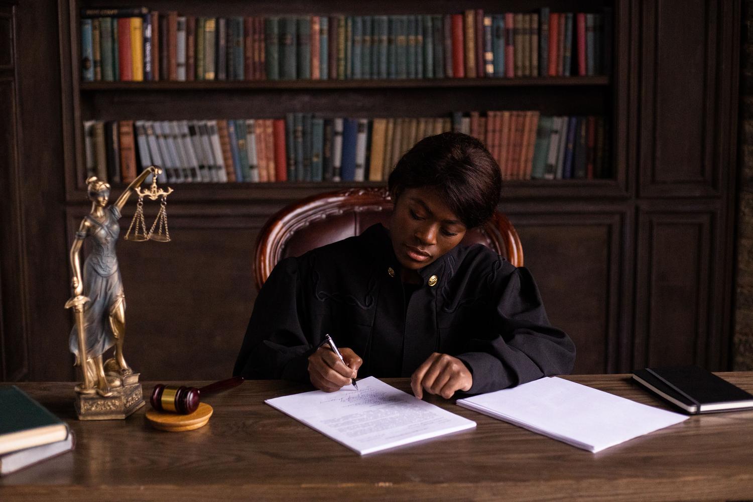 Profesional con toga judicial escribiendo en una biblioteca jurídica, representando el máximo grado de capacitación intelectual y éxito profesional. Profesional con toga judicial escribiendo en una biblioteca jurídica, representando el máximo grado de capacitación intelectual y éxito profesional.