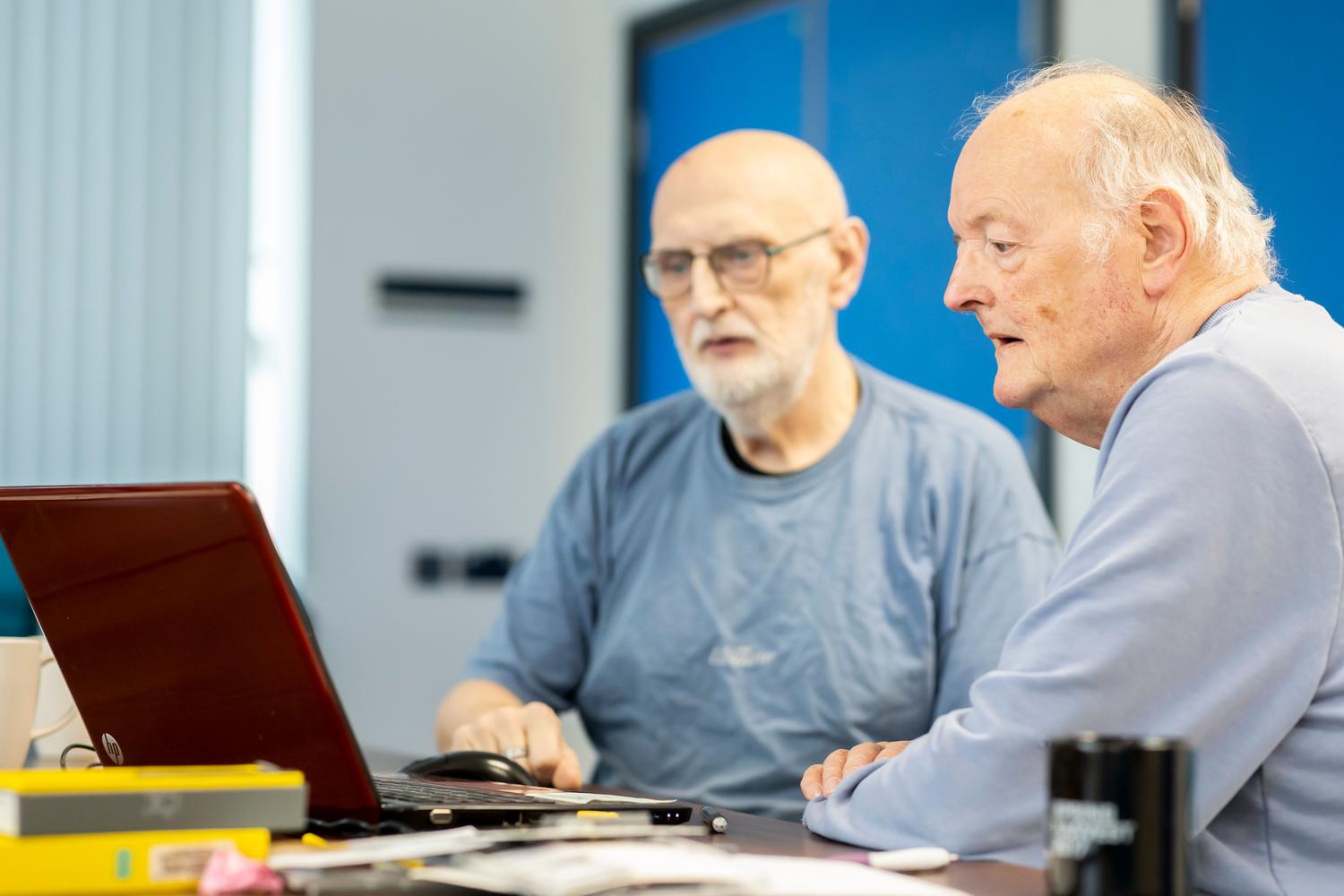 Peer-to-peer learning Two elderly men collaborating while working on a laptop, showcasing peer-to-peer learning and technology adoption among seniors.