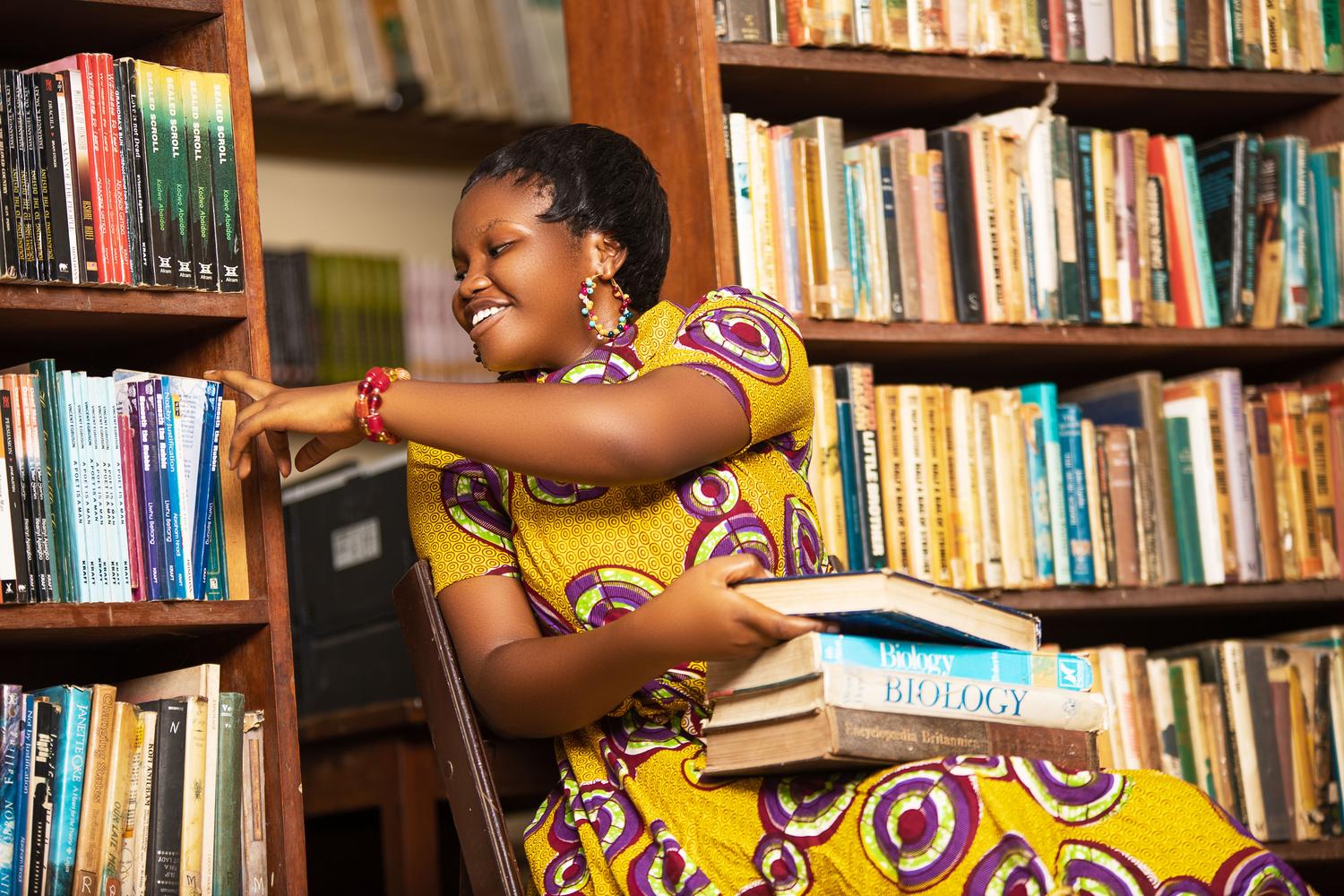 Empowerment through education Smiling African woman reading books in a Ghanaian library, symbolizing the empowerment of women through education and literacy.