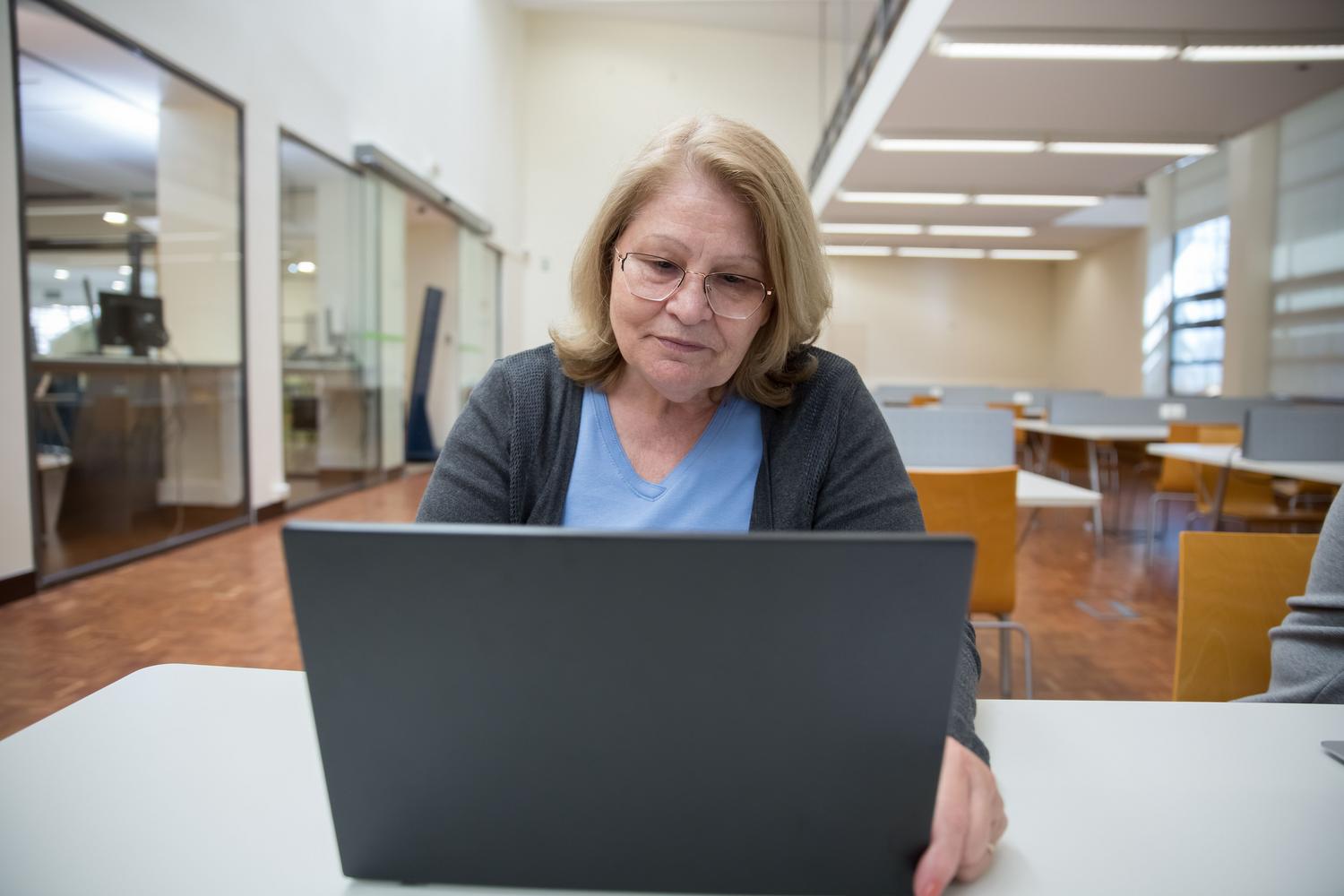 Individual lifelong education Elderly woman focused on learning using a laptop in a spacious, modern library, illustrating the individual journey of lifelong education.