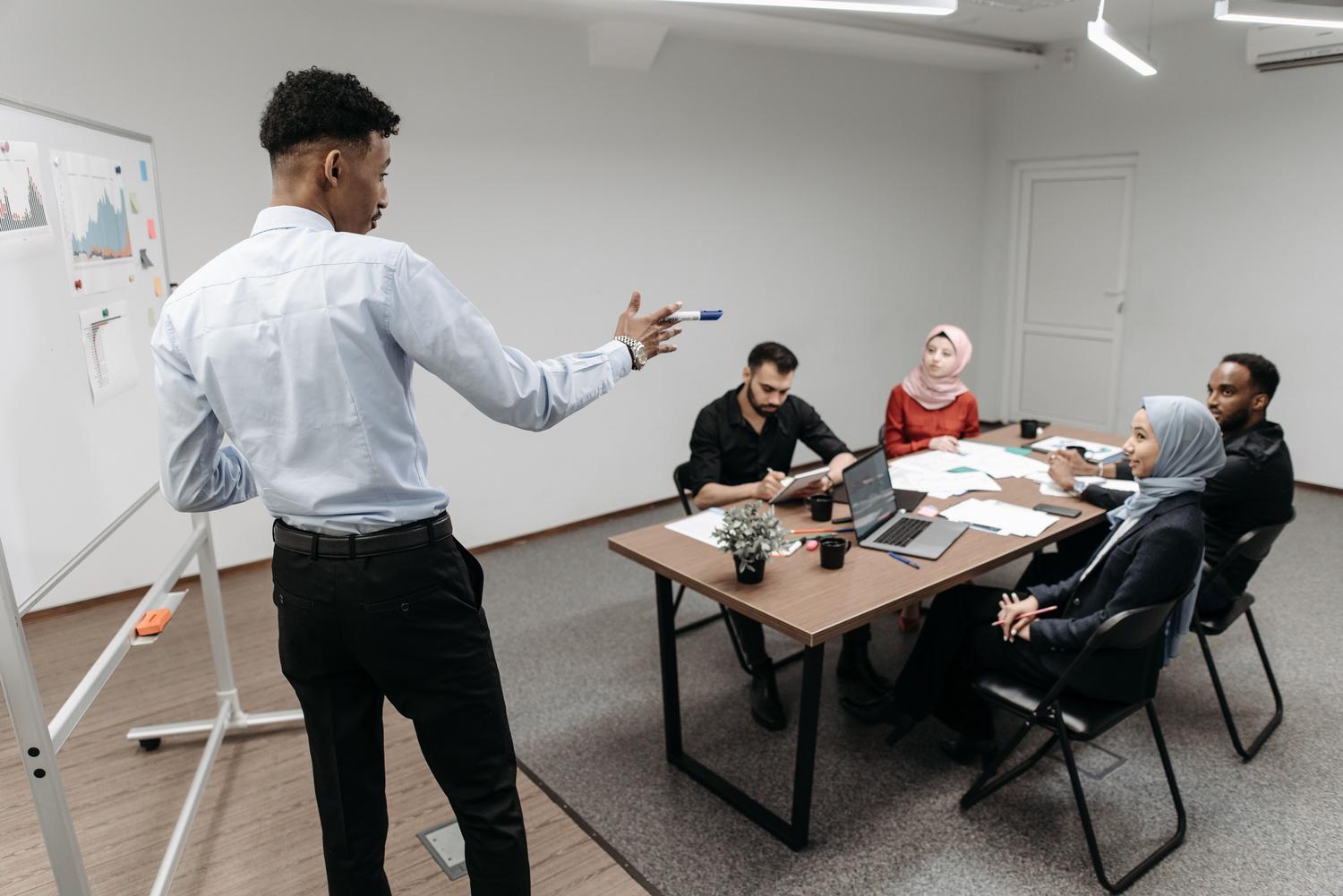 Discusión de estrategia Equipo multicultural de negocios discutiendo una estrategia frente a una pizarra con gráficos en una sala de juntas.