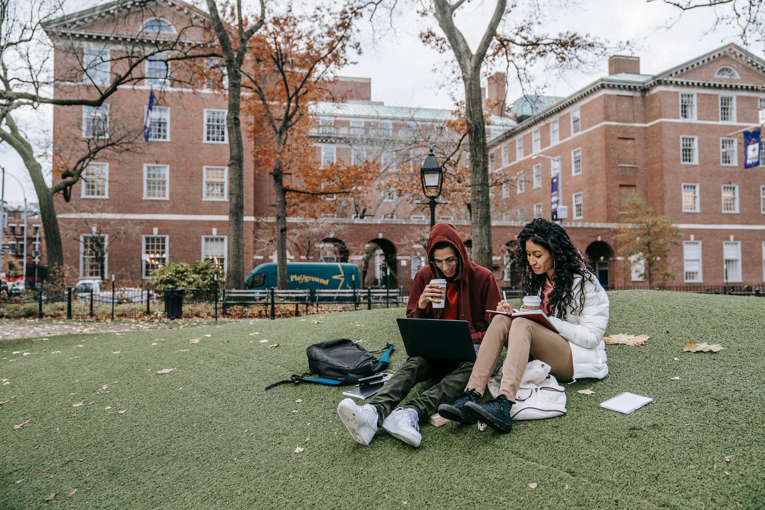 Estudiantes utilizando ordenadores portátiles y cuadernos en el campus, representando el uso de recursos digitales y bancos de apuntes. Estudiantes utilizando ordenadores portátiles y cuadernos en el campus, representando el uso de recursos digitales y bancos de apuntes.
