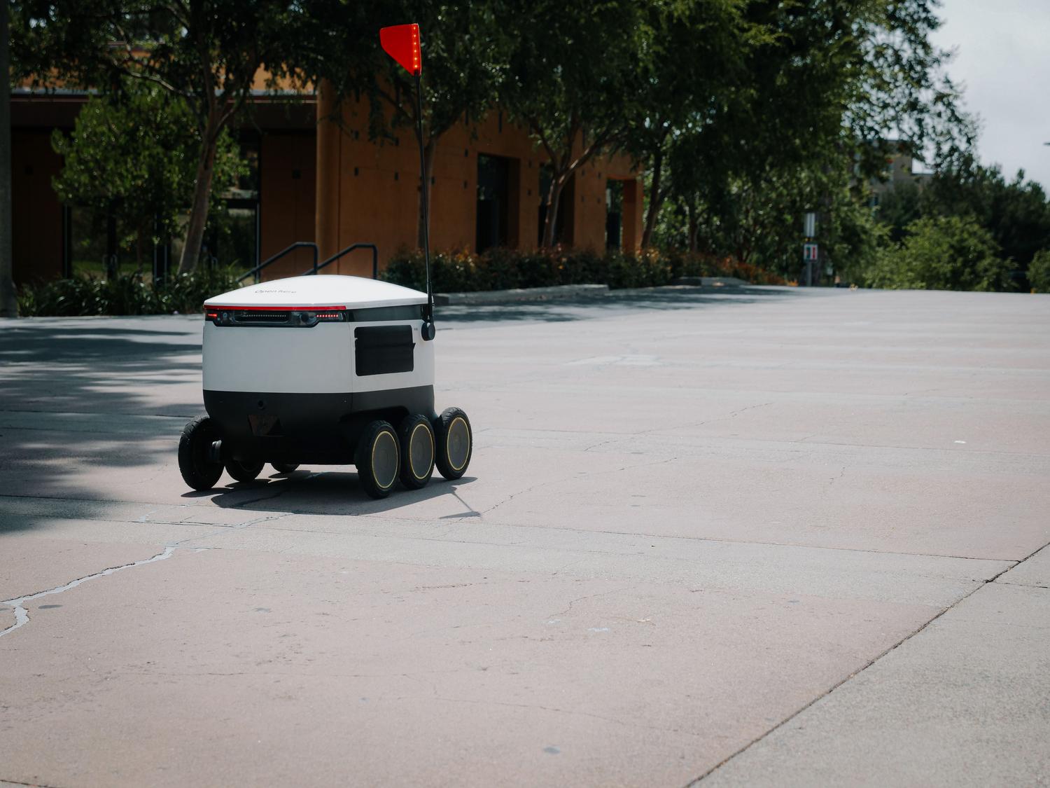 Robot autónomo de reparto de comida navegando por una ciudad, ejemplo de los AMRs (Robots Móviles Autónomos) aplicados a la logística. Robot autónomo de reparto de comida navegando por una ciudad, ejemplo de los AMRs (Robots Móviles Autónomos) aplicados a la logística.