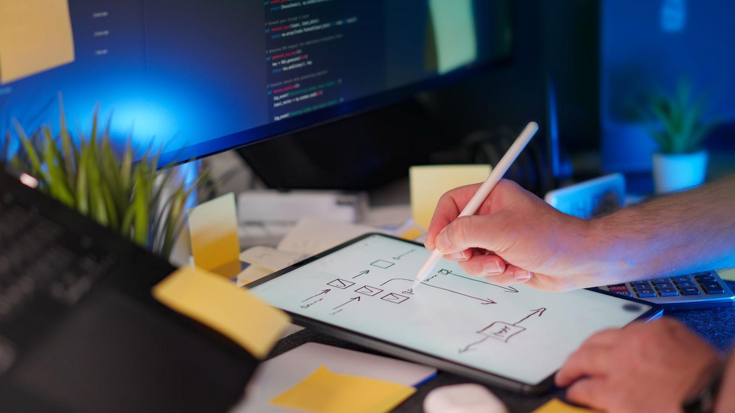 Espacio de trabajo tecnológico con una persona dibujando flujos lógicos en una tablet mientras un monitor muestra código, representando el flujo de trabajo híbrido del Vibe Coding. Espacio de trabajo tecnológico con una persona dibujando flujos lógicos en una tablet mientras un monitor muestra código, representando el flujo de trabajo híbrido del Vibe Coding.