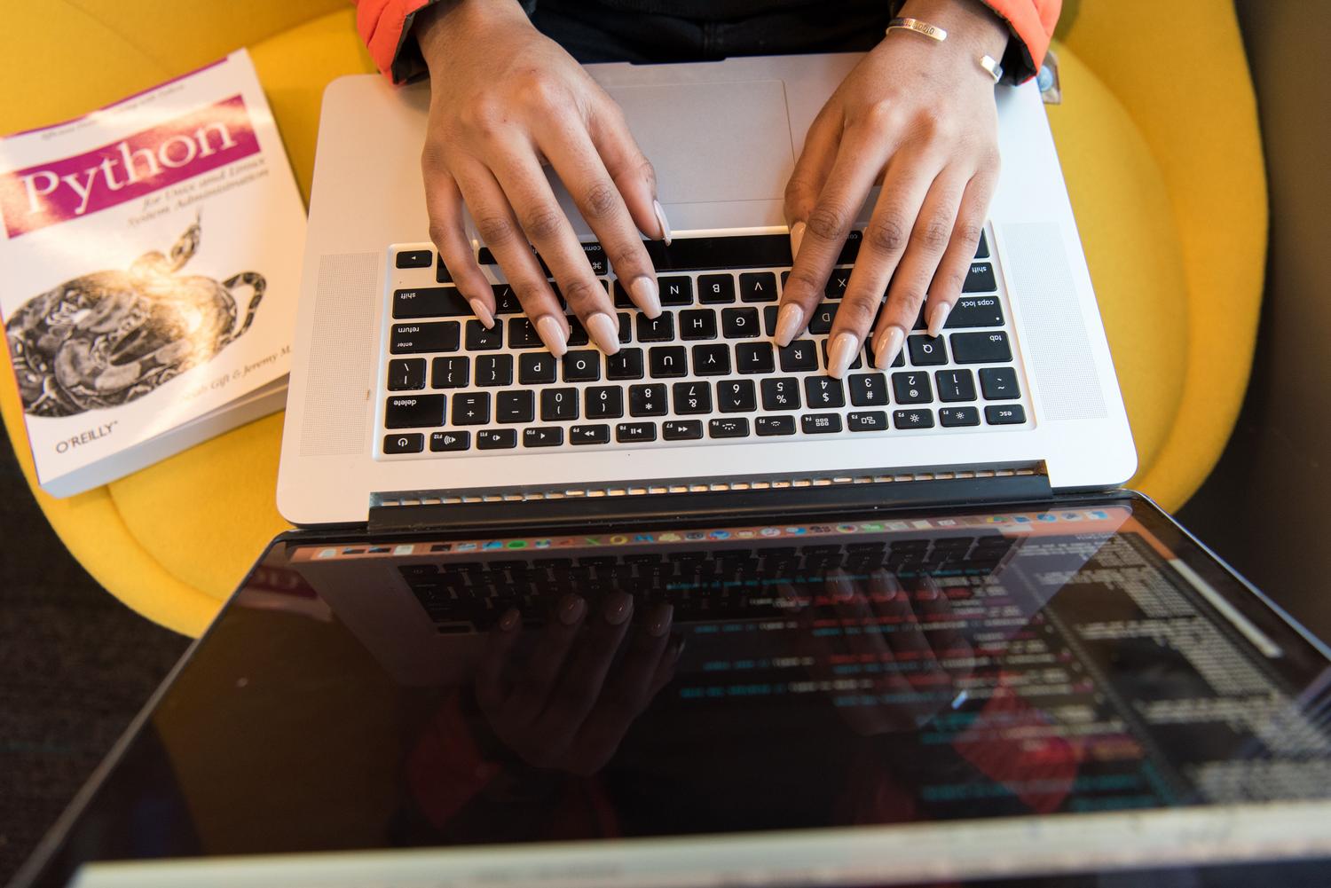 Formazione tecnica e lingue essenziali Primo piano di mani che programmano su un laptop con un libro di Python accanto, a illustrare la formazione tecnica e i linguaggi di programmazione essenziali.