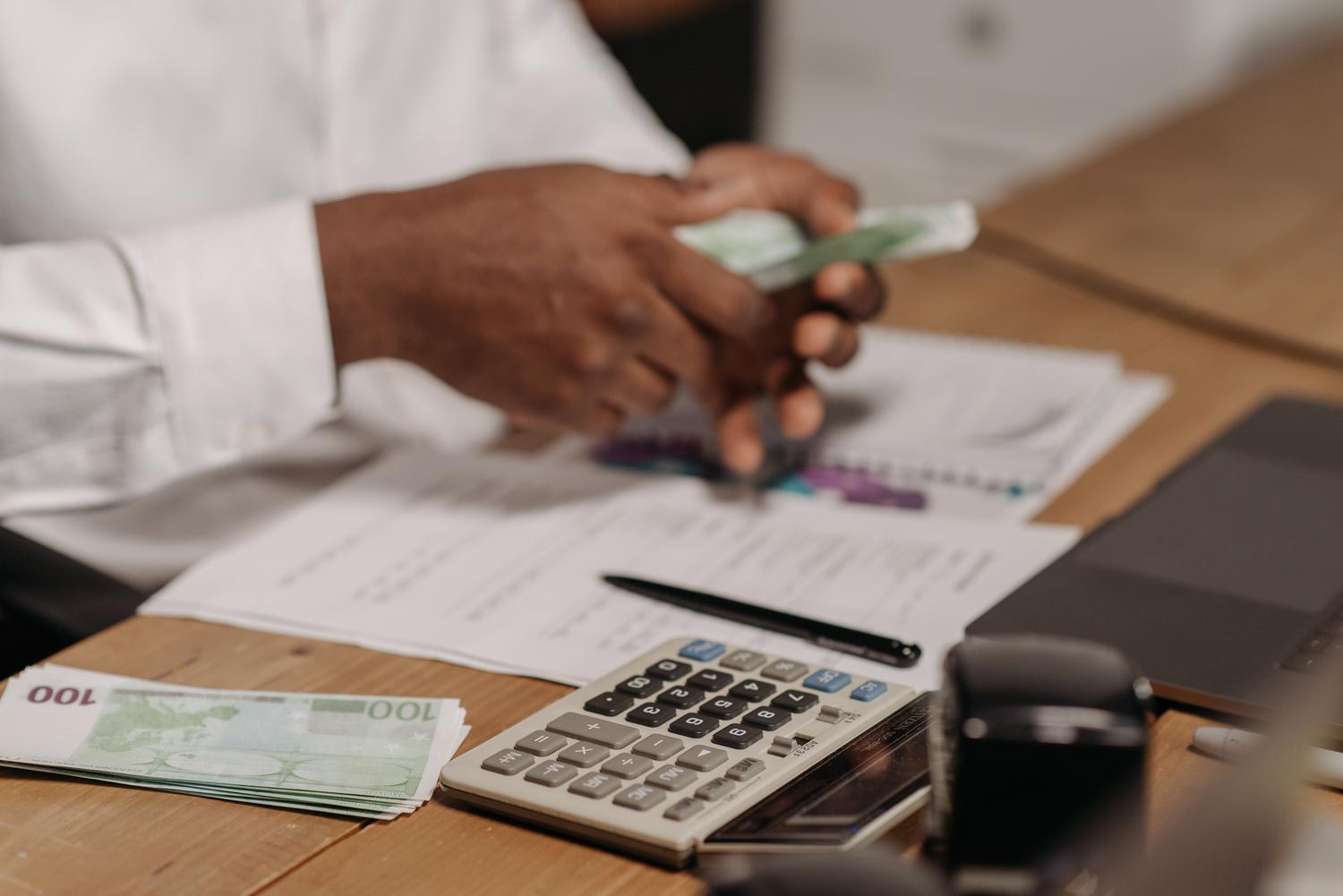Primer plano de manos contando billetes de euro con una calculadora, ilustrando la gestión de ingresos y gastos del autónomo. Primer plano de manos contando billetes de euro con una calculadora, ilustrando la gestión de ingresos y gastos del autónomo.