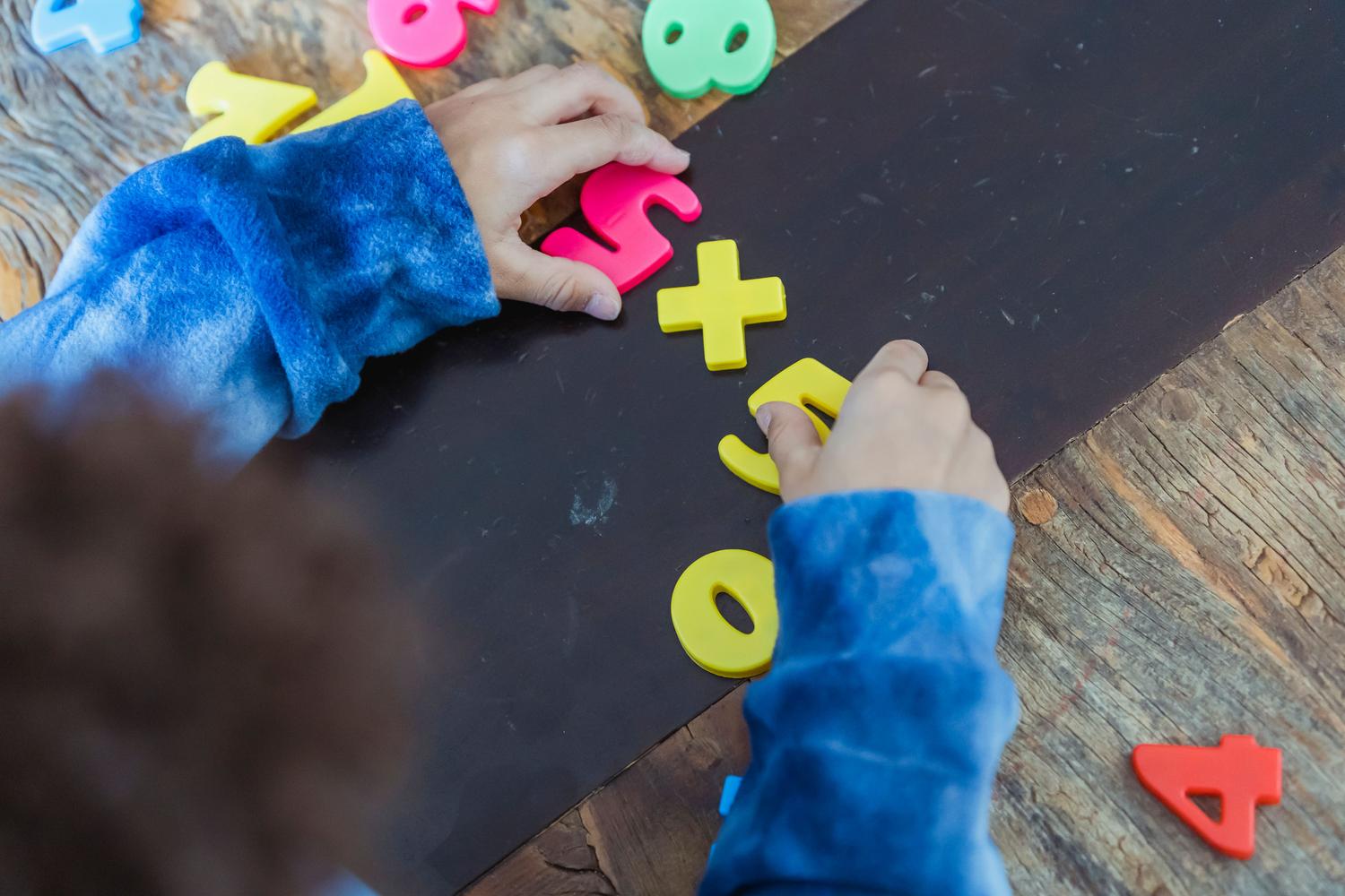 Estudiante de primaria resolviendo una operación de multiplicación con números de plástico coloridos sobre una mesa Estudiante de primaria resolviendo una operación de multiplicación con números de plástico coloridos sobre una mesa