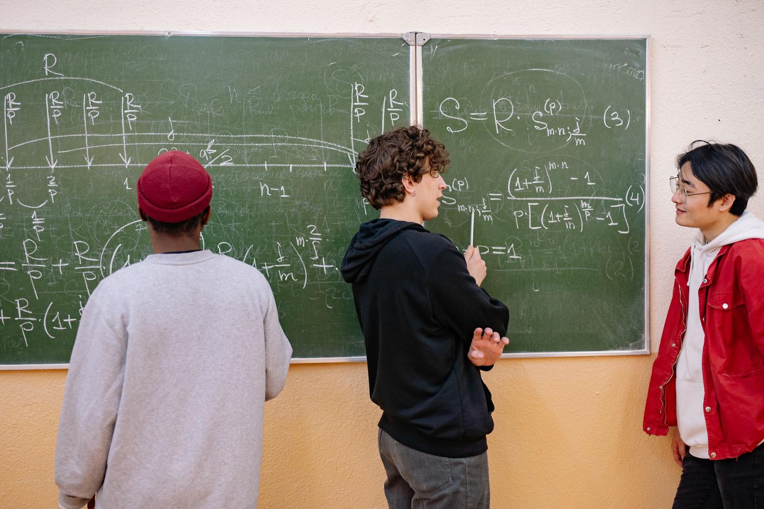 Grupo de estudiantes de secundaria discutiendo y resolviendo ecuaciones matemáticas complejas en una pizarra Grupo de estudiantes de secundaria discutiendo y resolviendo ecuaciones matemáticas complejas en una pizarra
