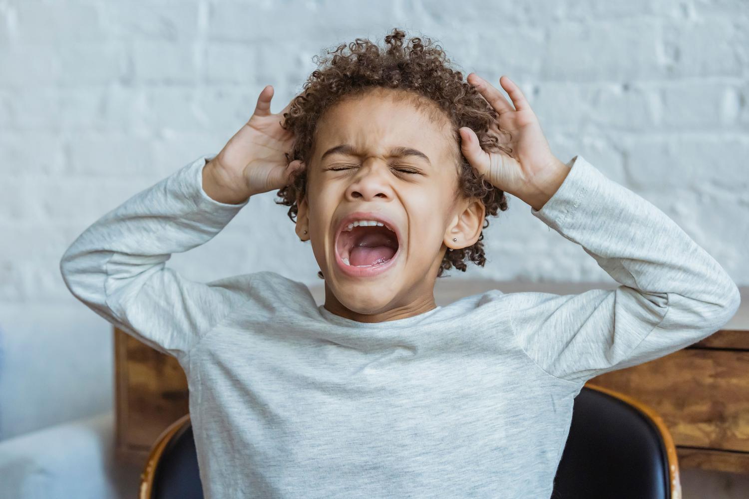 Niño pequeño gritando en un momento de crisis emocional o meltdon, agarrándose la cabeza con frustración. Niño pequeño gritando en un momento de crisis emocional o meltdon, agarrándose la cabeza con frustración.