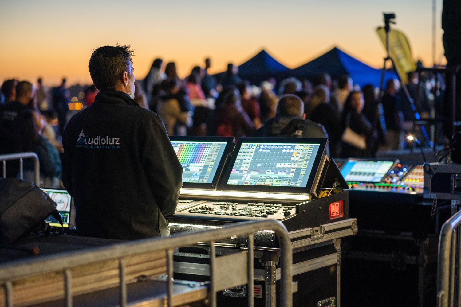 Técnico de sonido gestionando la mesa de mezclas y paneles de iluminación en un evento al aire libre durante el atardecer. Técnico de sonido gestionando la mesa de mezclas y paneles de iluminación en un evento al aire libre durante el atardecer.