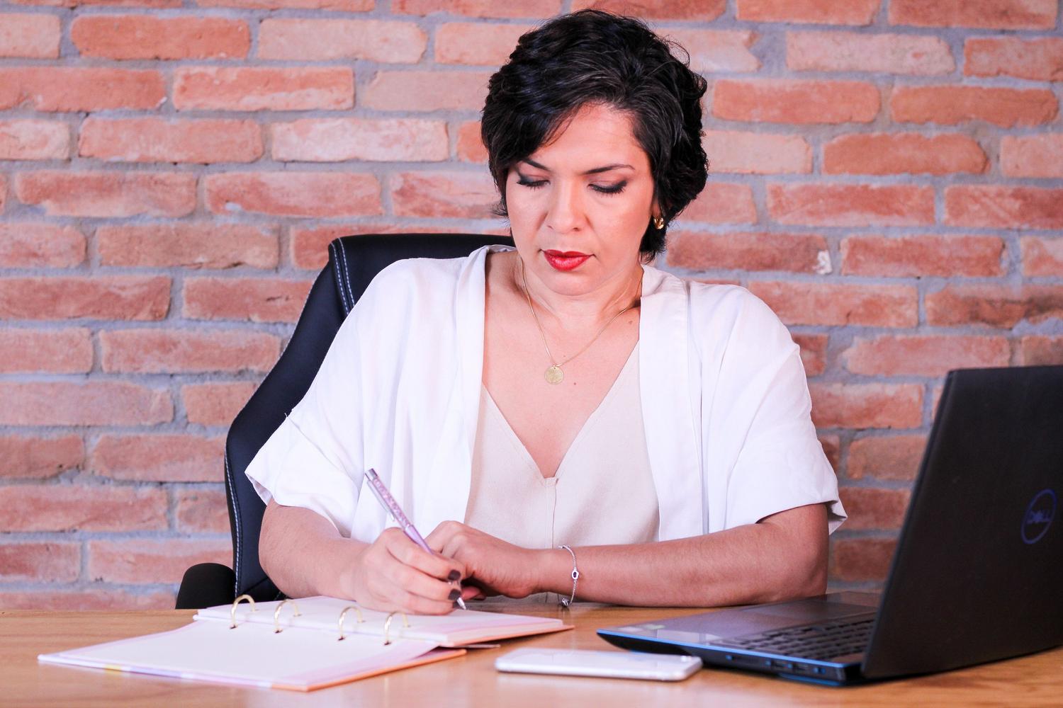 Mujer emprendedora organizando su plan de empresa en un cuaderno y ordenador portátil Mujer emprendedora organizando su plan de empresa en un cuaderno y ordenador portátil
