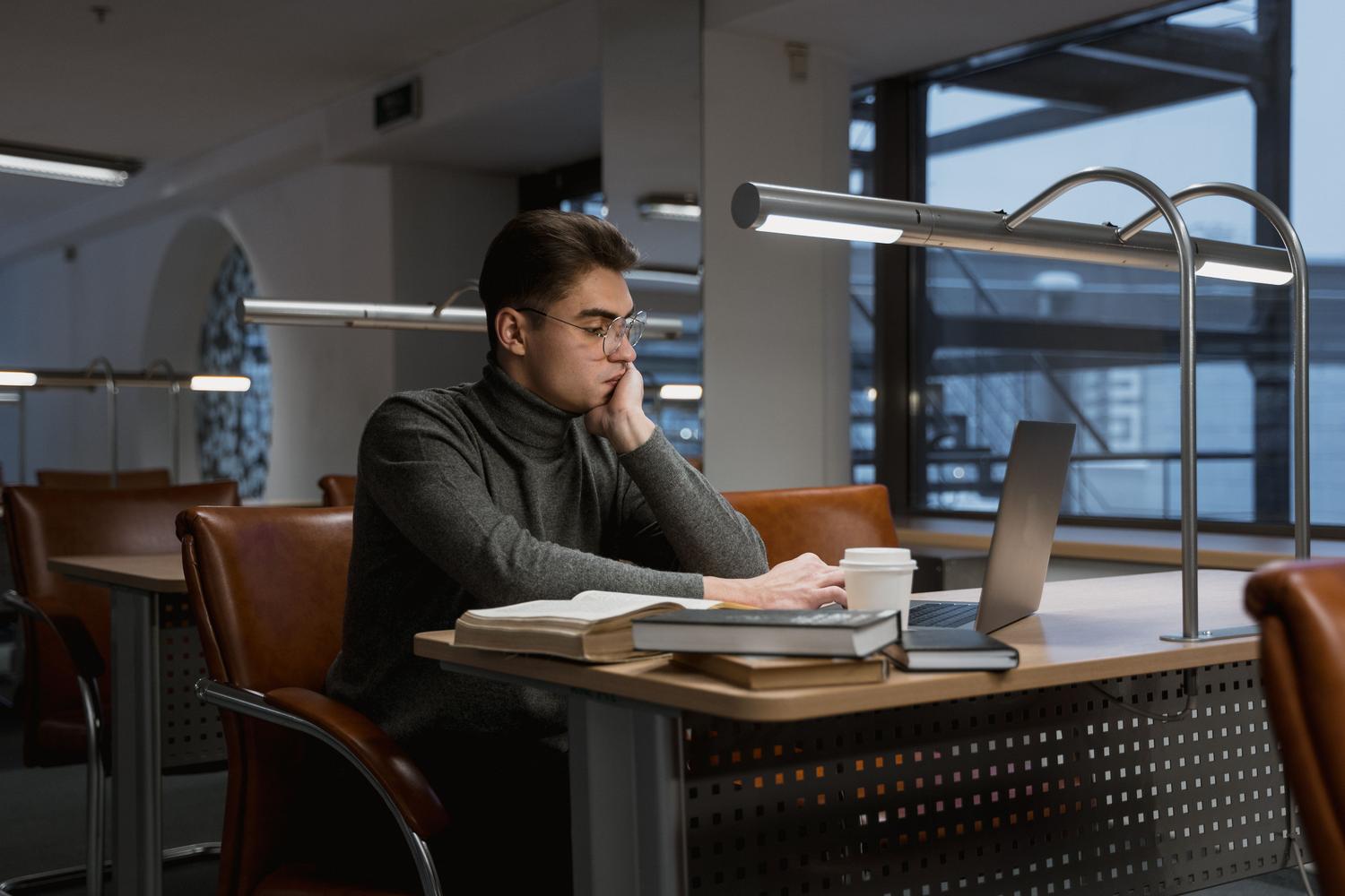 Specialized student working with laptop and books in a modern library, representing the acquisition of technical skills. Specialized student working with laptop and books in a modern library, representing the acquisition of technical skills.