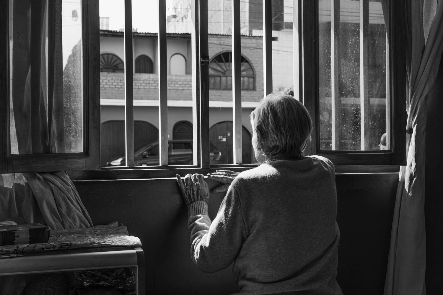 Mujer mayor mirando por la ventana en actitud contemplativa, reflejando la vulnerabilidad y soledad asociada a la viudedad. Mujer mayor mirando por la ventana en actitud contemplativa, reflejando la vulnerabilidad y soledad asociada a la viudedad.
