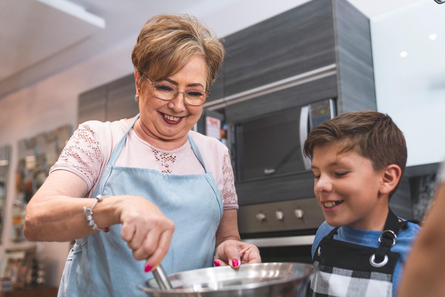 Abuela y nieto cocinando juntos en una cocina moderna, ejemplificando las cargas familiares que afectan la cuantía de la pensión. Abuela y nieto cocinando juntos en una cocina moderna, ejemplificando las cargas familiares que afectan la cuantía de la pensión.