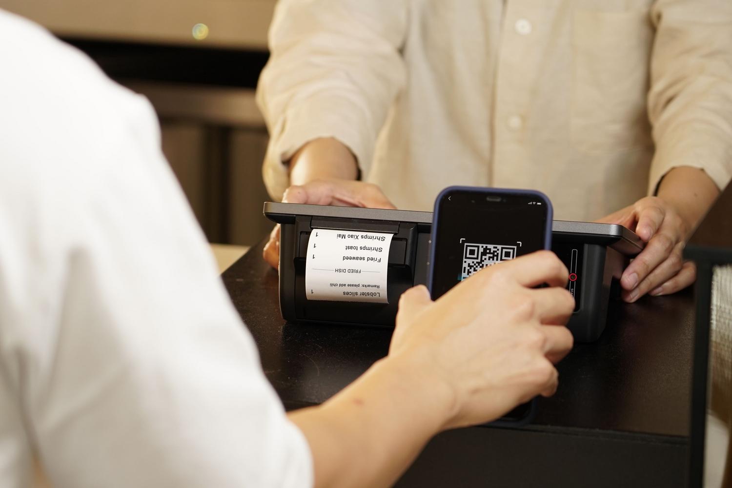 Persona realizando un pago móvil escaneando un código QR en el mostrador de una tienda Persona realizando un pago móvil escaneando un código QR en el mostrador de una tienda
