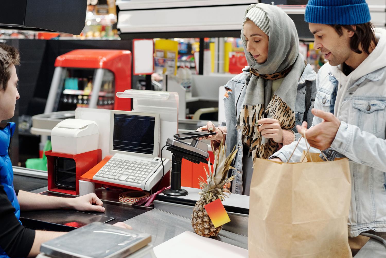 Cliente utilizando el móvil para pagar en la caja de un supermercado Cliente utilizando el móvil para pagar en la caja de un supermercado