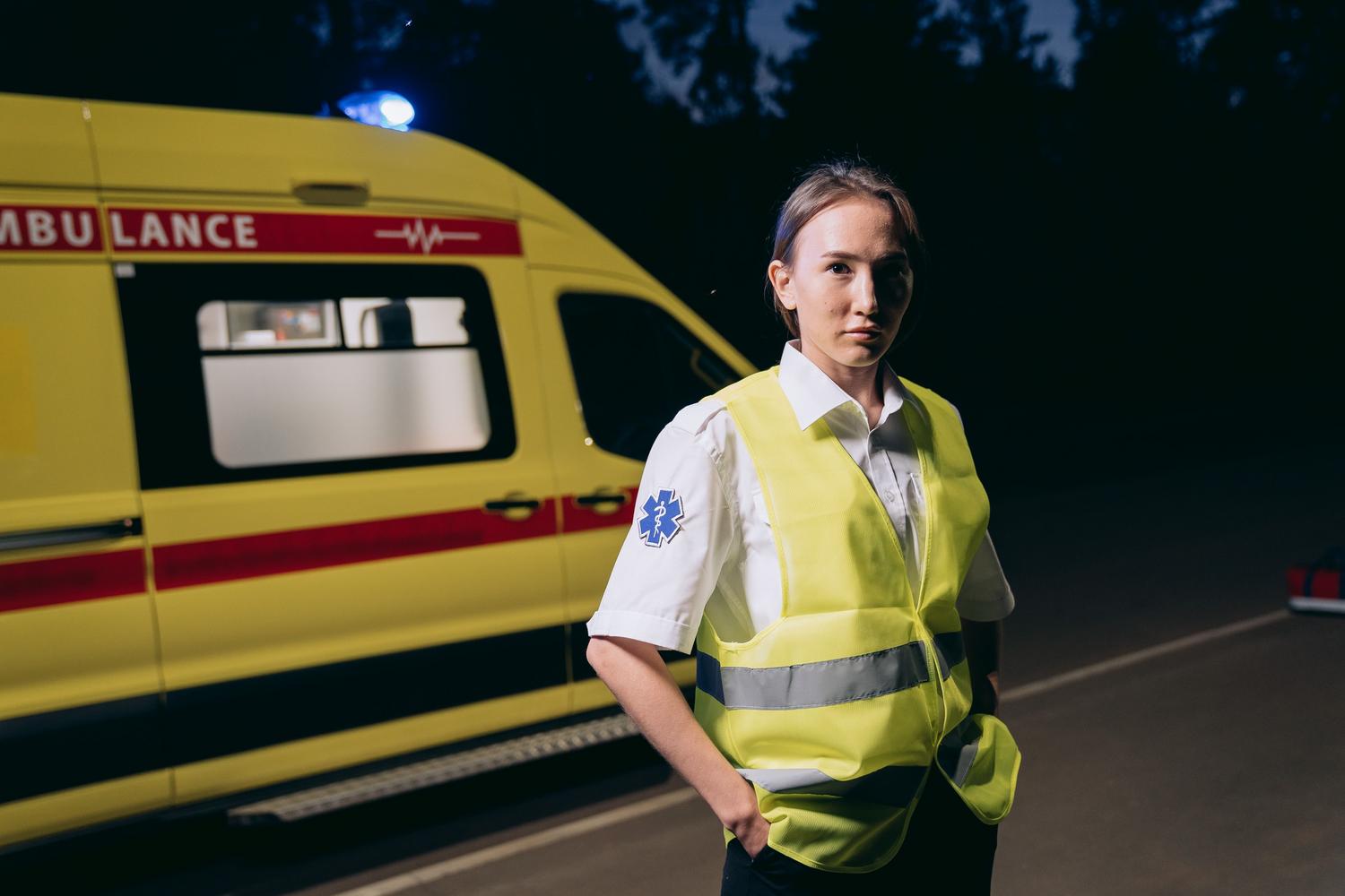 Paramédica con chaleco reflectante junto a una ambulancia en una calle de la ciudad durante la noche. Paramédica con chaleco reflectante junto a una ambulancia en una calle de la ciudad durante la noche.