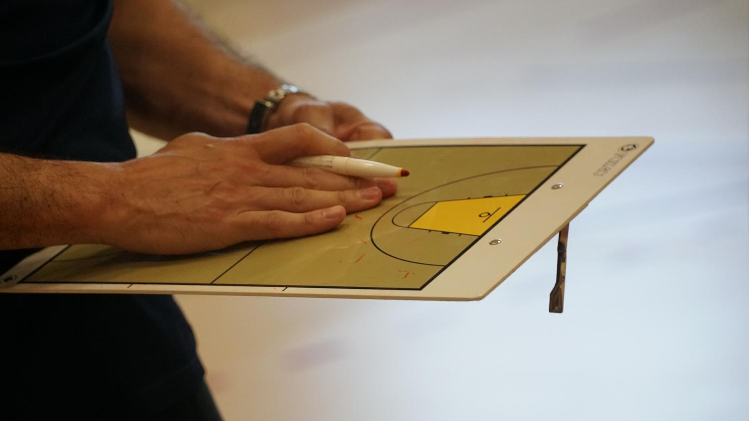 Entrenador utilizando una pizarra táctica de baloncesto Entrenador utilizando una pizarra táctica de baloncesto para planificar la estrategia, representando la gestión y administración deportiva.