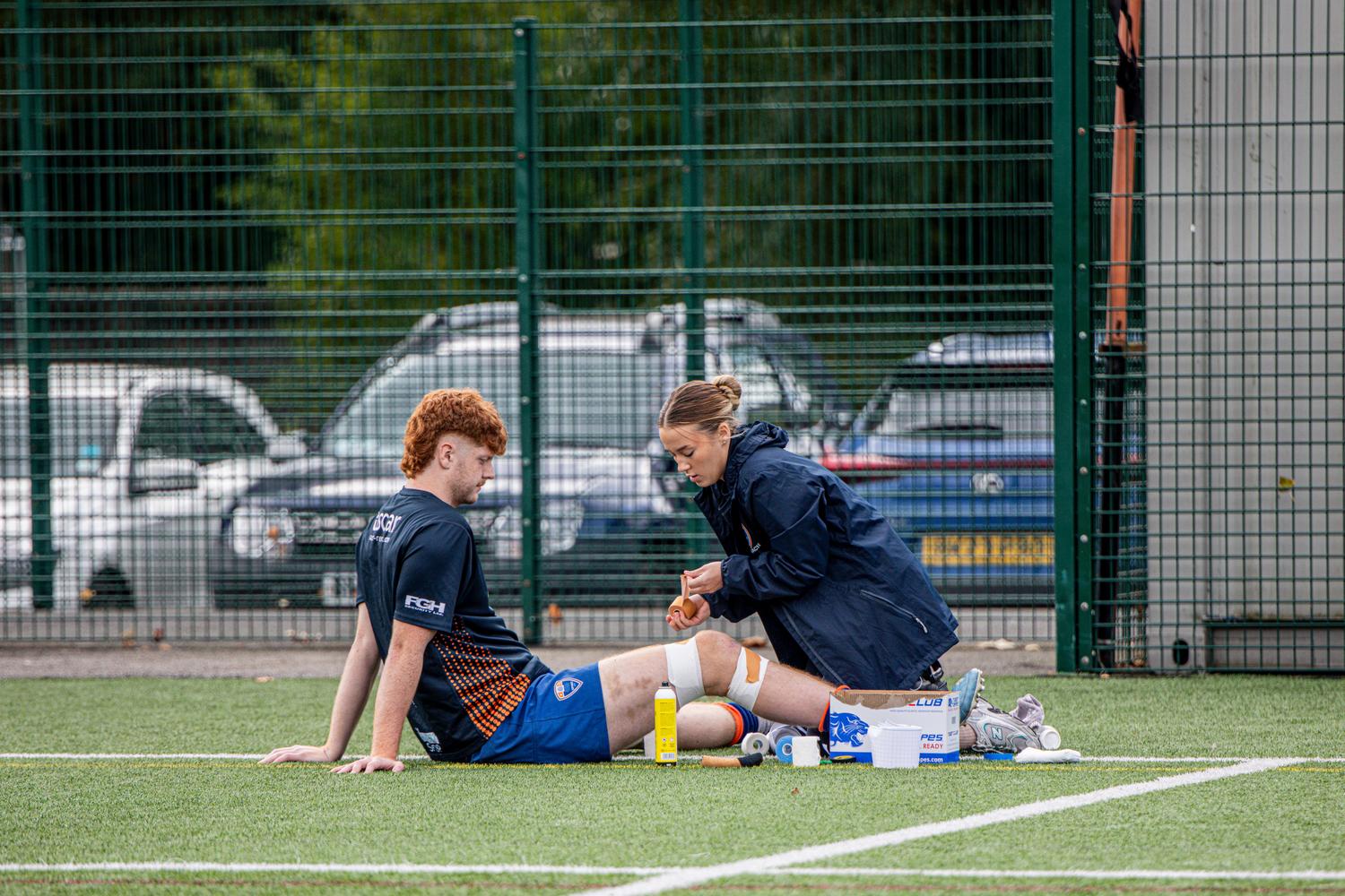 Fisioterapeuta deportivo tratando a un atleta lesionado Fisioterapeuta deportivo tratando a un atleta lesionado en un campo de fútbol, ilustrando la especialización en salud y rehabilitación.