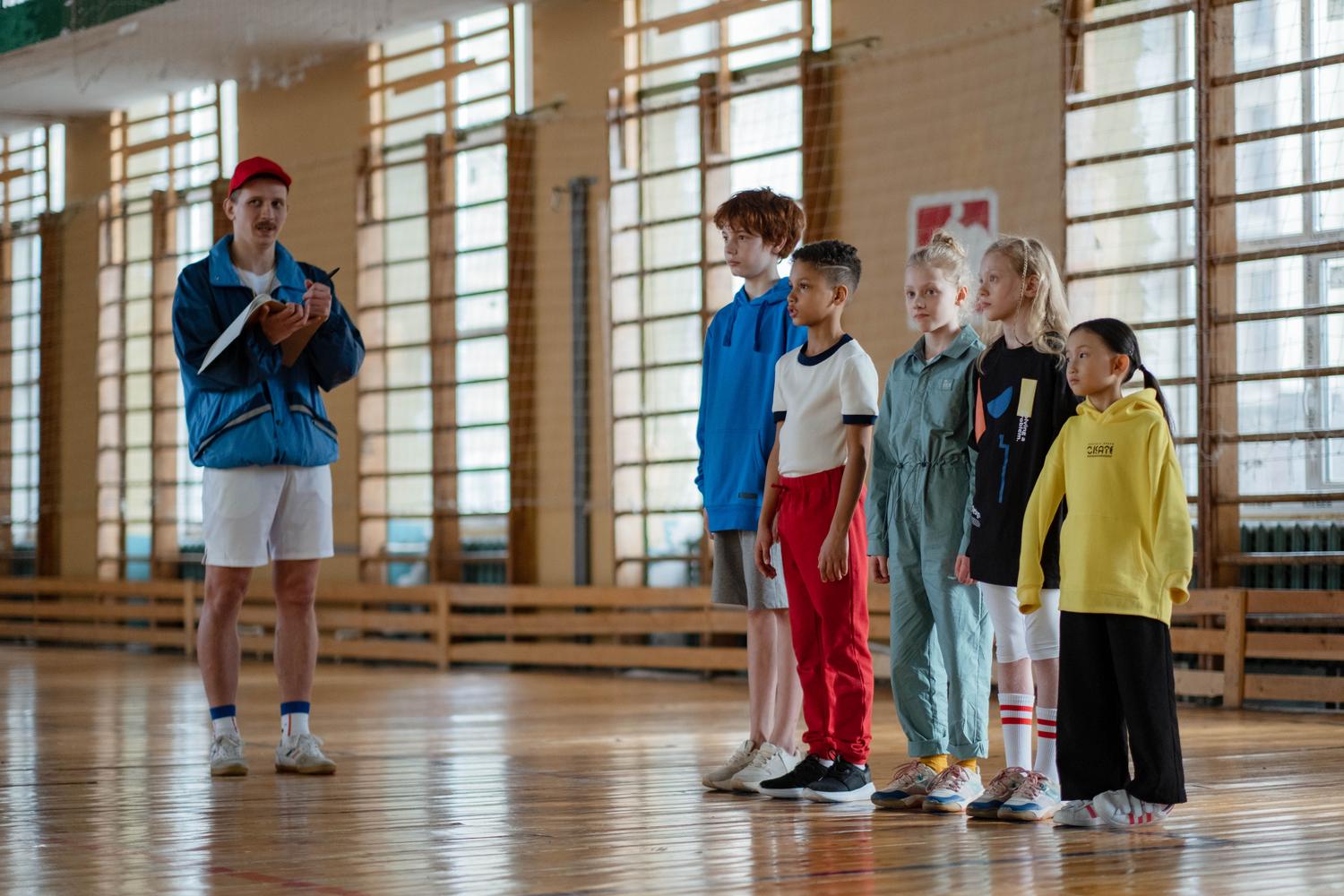 Profesor de educación física impartiendo clase a un grupo de niños Profesor de educación física impartiendo clase a un grupo de niños en el gimnasio escolar, enfocado en la formación de base y pedagogía.