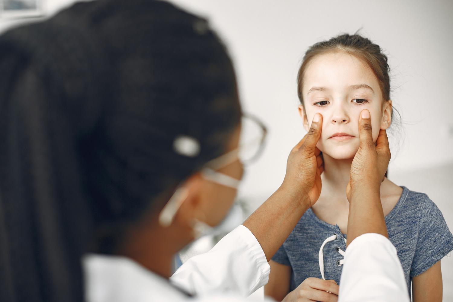 Dermatología infantil y revisión pediátrica Pediatra examinando cuidadosamente el rostro de una niña durante una revisión médica.