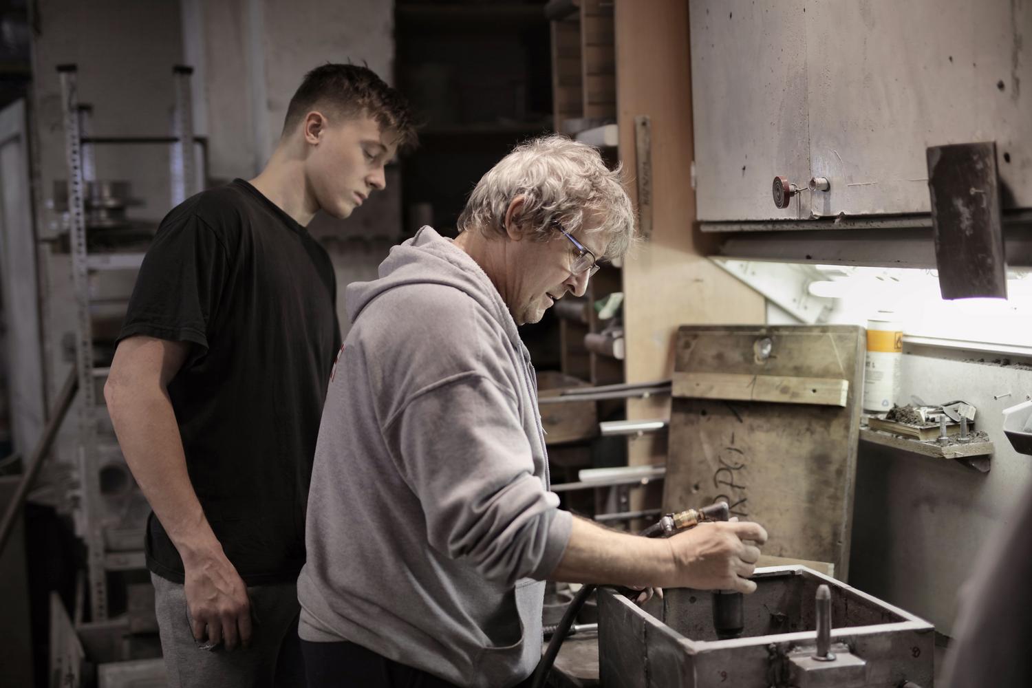 Un trabajador experimentado enseñando a un joven aprendiz en un taller, ejemplificando los modelos de mentoría e inmersión laboral para jóvenes. Un trabajador experimentado enseñando a un joven aprendiz en un taller, ejemplificando los modelos de mentoría e inmersión laboral para jóvenes.