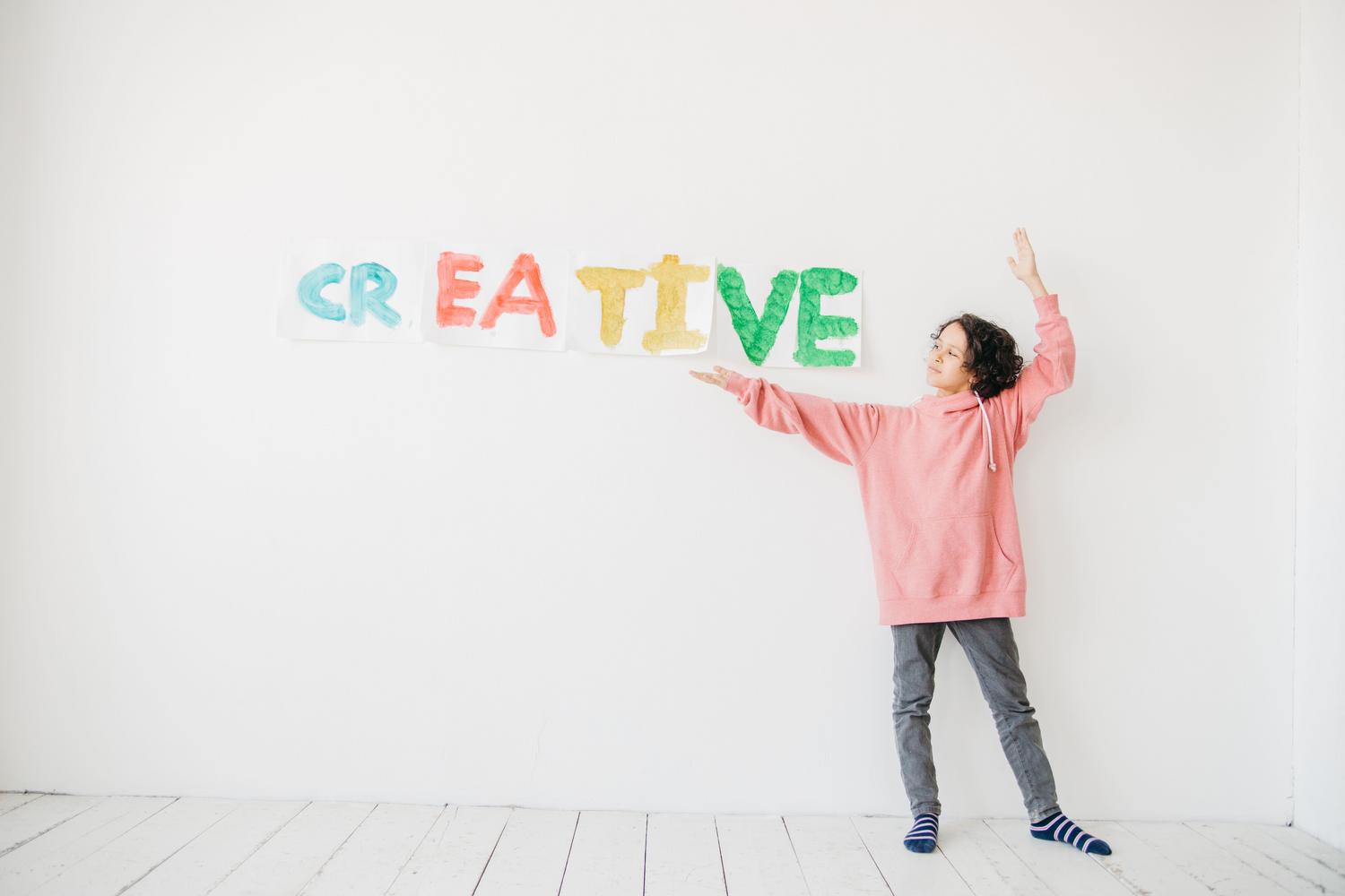 Un niño señalando la palabra 'CREATIVE' en una pared, vinculando la creatividad con el entorno educativo. Un niño señalando la palabra 'CREATIVE' en una pared, vinculando la creatividad con el entorno educativo.