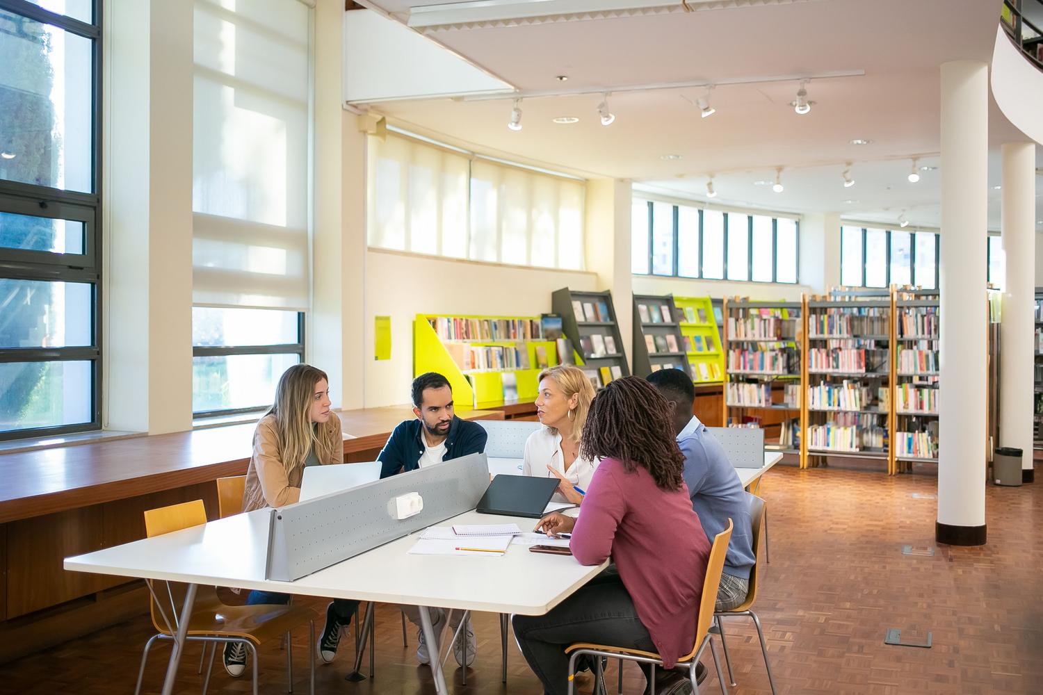 Grupo diverso de estudiantes universitarios trabajando con ordenadores y documentos en una biblioteca, gestionando solicitudes de ayudas. Grupo diverso de estudiantes universitarios trabajando con ordenadores y documentos en una biblioteca, gestionando solicitudes de ayudas.
