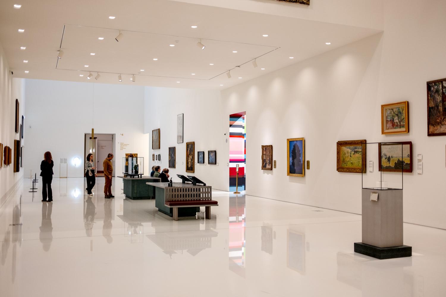 Interior de un museo de arte moderno con visitantes contemplando las obras, representando los centros de formación práctica en gestión cultural. Interior de un museo de arte moderno con visitantes contemplando las obras, representando los centros de formación práctica en gestión cultural.