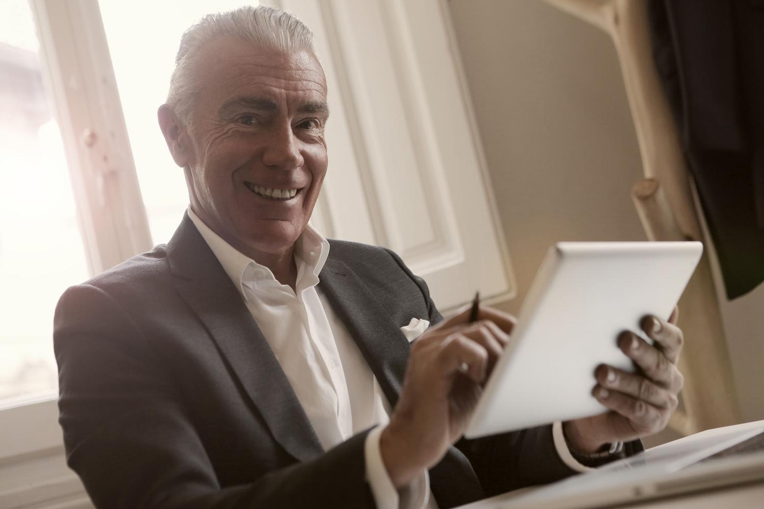 Empresario senior sonriente utilizando una tablet en un despacho moderno, representando la jubilación activa. Empresario senior sonriente utilizando una tablet en un despacho moderno, representando la jubilación activa.