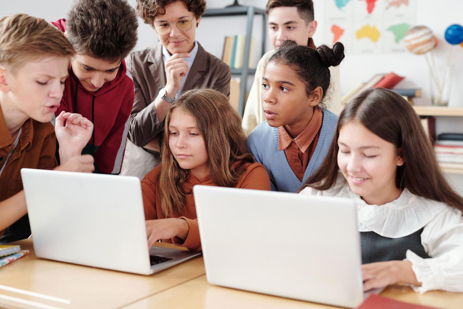 Competencias mediáticas e informacionales Estudiantes de secundaria colaborando con ordenadores portátiles en un aula moderna, reflejando la adquisición de competencias digitales.