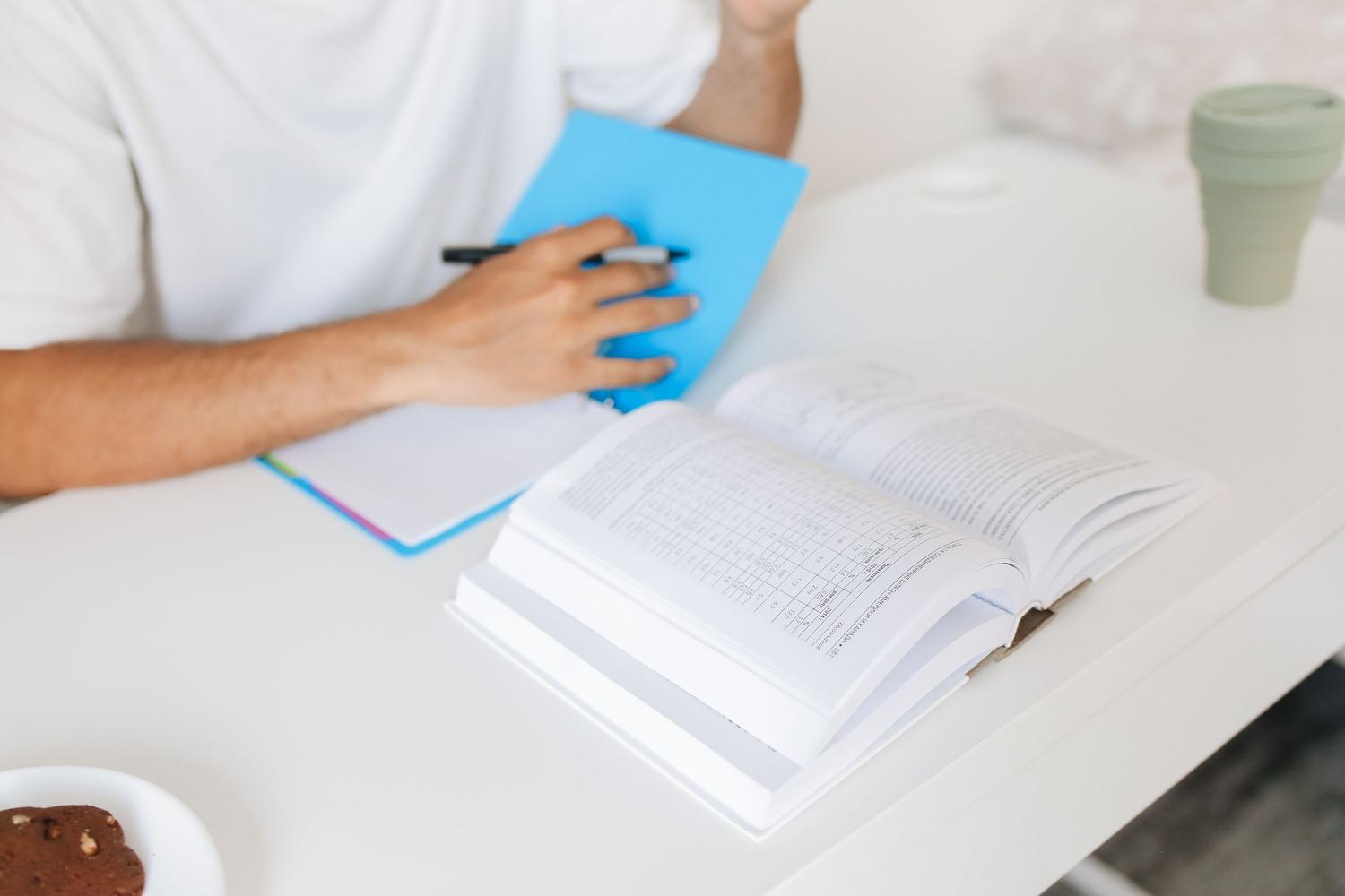 Adult person concentrating on studying with books and notebook at a desk, representing preparation for competitive exams. Adult person concentrating on studying with books and notebook at a desk, representing preparation for competitive exams.